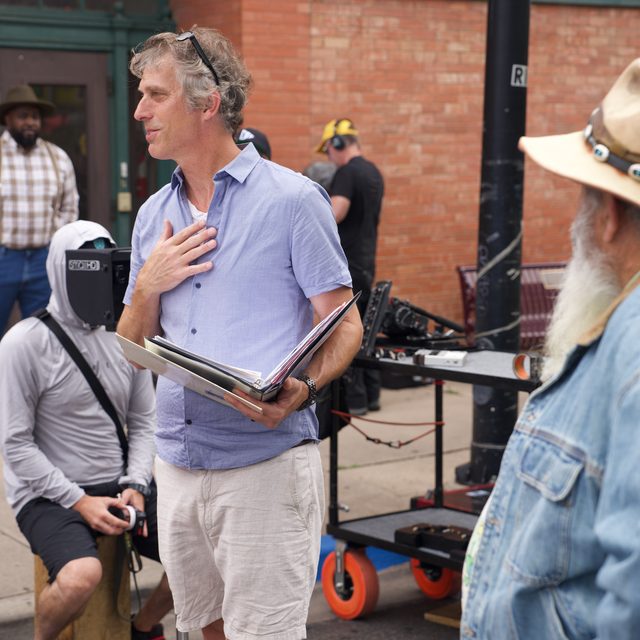 David on set with the script binder, talking to cast on a downtown street