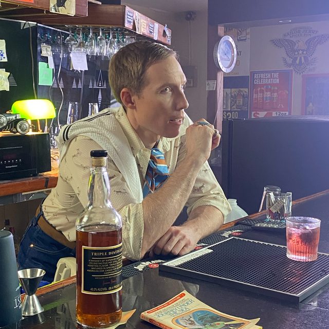 An actor in costume leans on the bar between takes