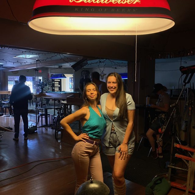 Two cast members under the Budweiser lamp between setups