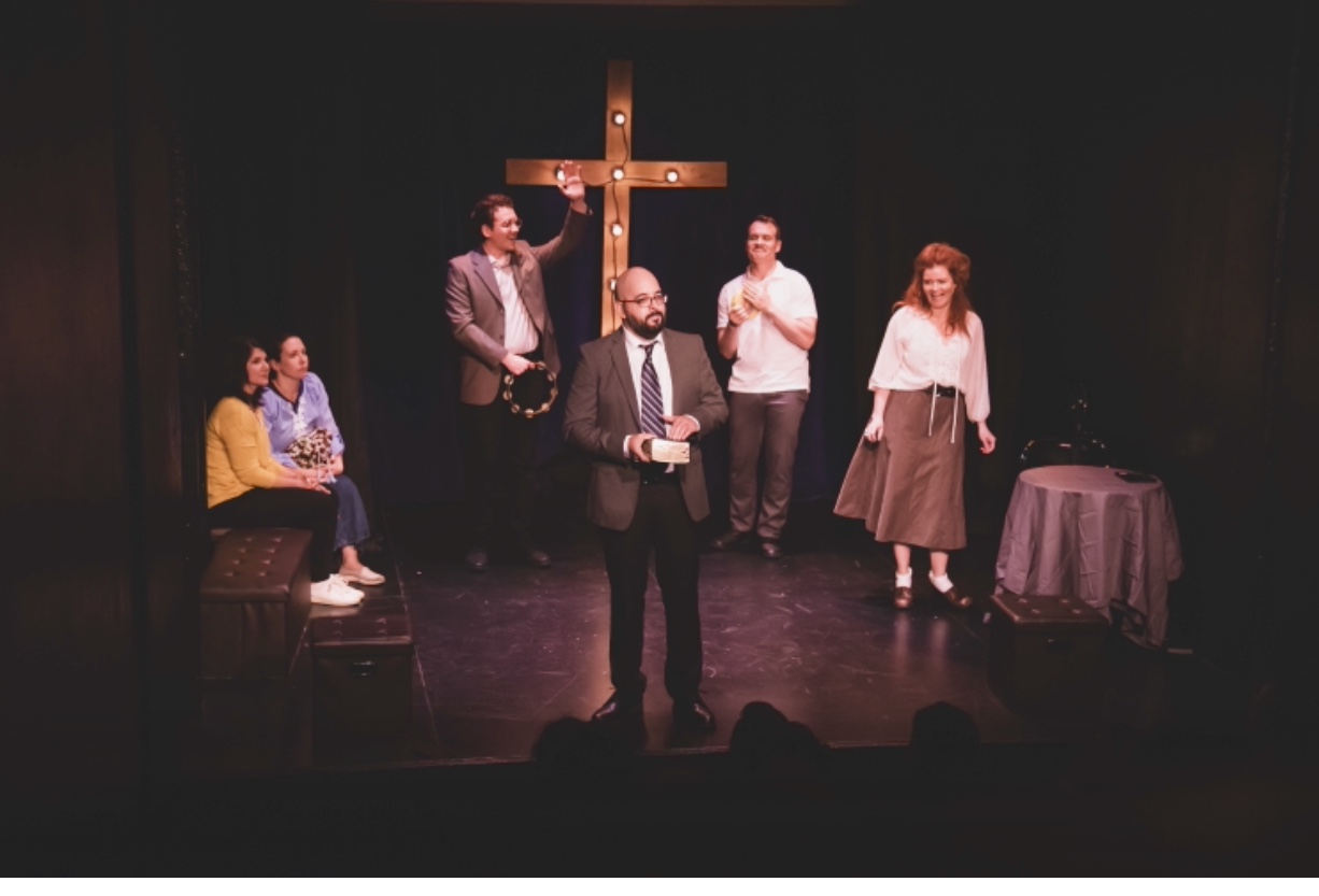 The cast of Saving Cain on a dark stage beneath a lit cross